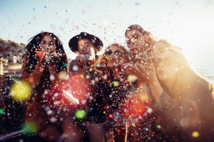 Teenager hipster friends celebrating by blowing colorful confetti from hands